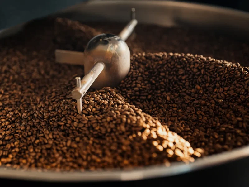 High angle of aromatic freshly roasted coffee beans in large cooling tray of roasting machine at factory